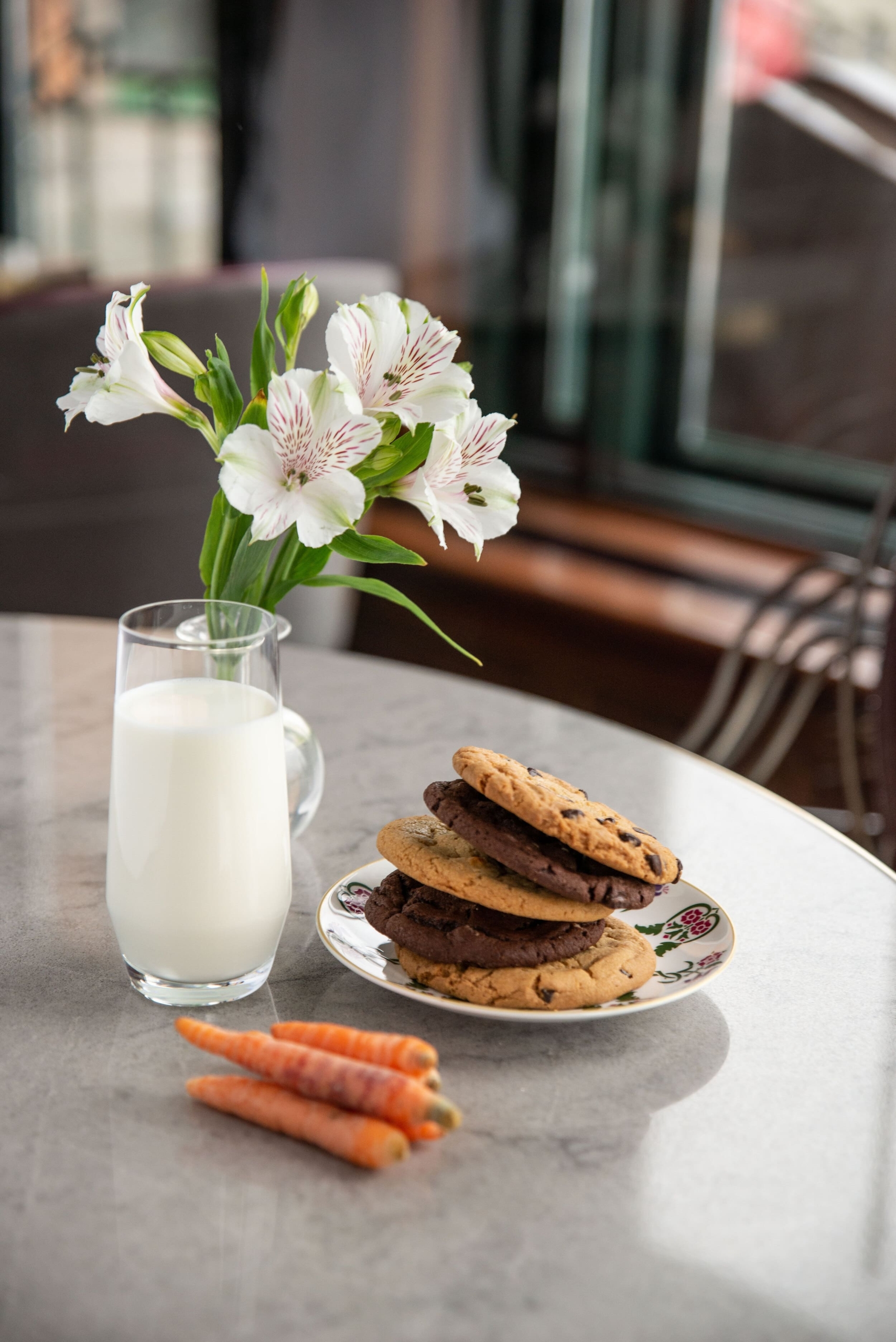 a glass of milk and plate of cookies with carrots on a table
